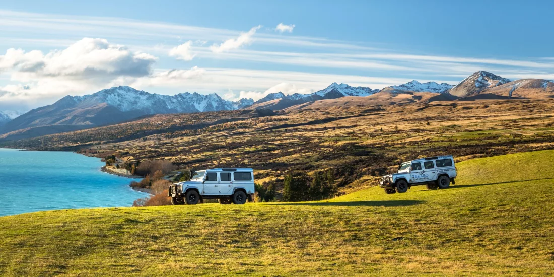 Two 4WD vehicles driving across Braemar Station with Lake Tekapo and snow-capped Southern Alps in the background