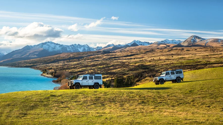 Two 4WD vehicles driving across Braemar Station with Lake Tekapo and snow-capped Southern Alps in the background