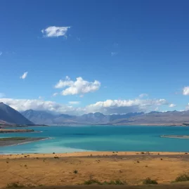 Lake Pukaki shining under blue skies, surrounded by dry grasslands and distant mountains