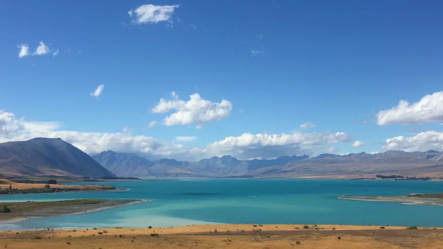 Lake Pukaki shining under blue skies, surrounded by dry grasslands and distant mountains