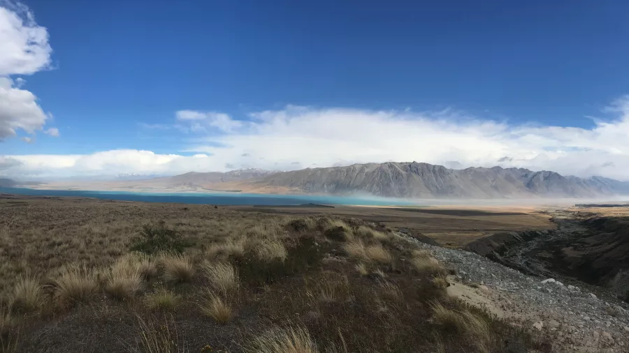 Expansive Mackenzie Basin with tussock grass, rugged hills, and distant turquoise lake