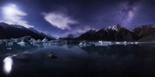 Night sky above Tasman Lake with icebergs and snowy peaks in Aoraki Mount Cook National Park