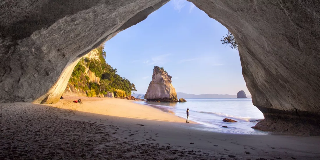 Sunrise view from inside Cathedral Cove’s natural arch, looking out towards the beach and Te Hoho Rock on the Coromandel Peninsula, New Zealand