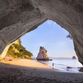 Sunrise view from inside Cathedral Cove’s natural arch, looking out towards the beach and Te Hoho Rock on the Coromandel Peninsula, New Zealand