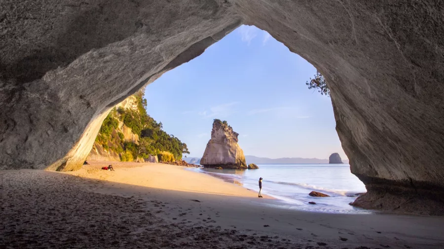 Sunrise view from inside Cathedral Cove’s natural arch, looking out towards the beach and Te Hoho Rock on the Coromandel Peninsula, New Zealand