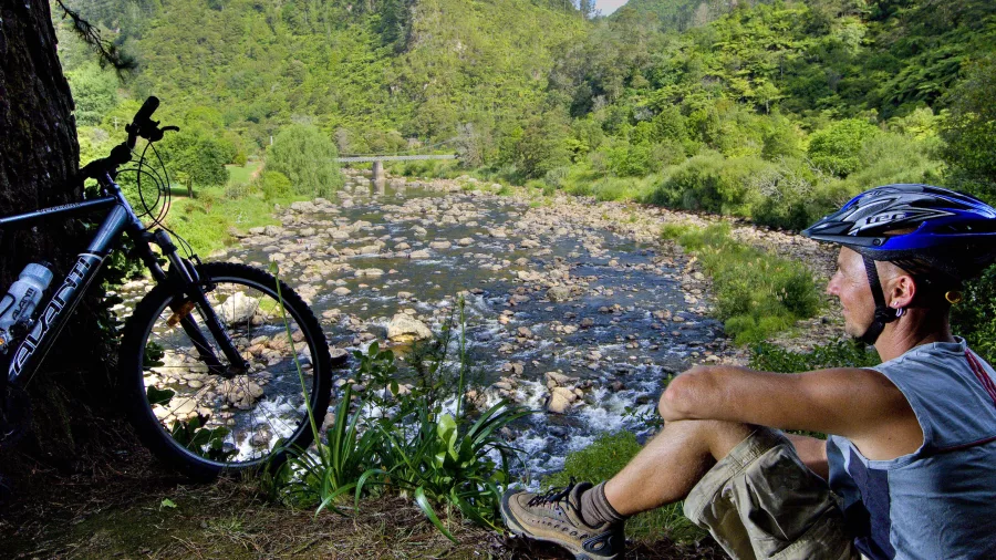 Cyclist resting by river in Karangahake Gorge