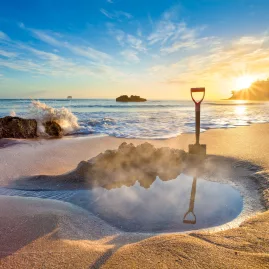 Steaming thermal pool dug into the sand at sunrise on Hot Water Beach, a famous geothermal attraction on the Coromandel Peninsula, New Zealand