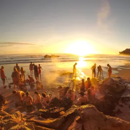 Crowds digging steaming thermal pools in the sand at sunrise on Hot Water Beach, a famous geothermal attraction on the Coromandel Peninsula, New Zealand