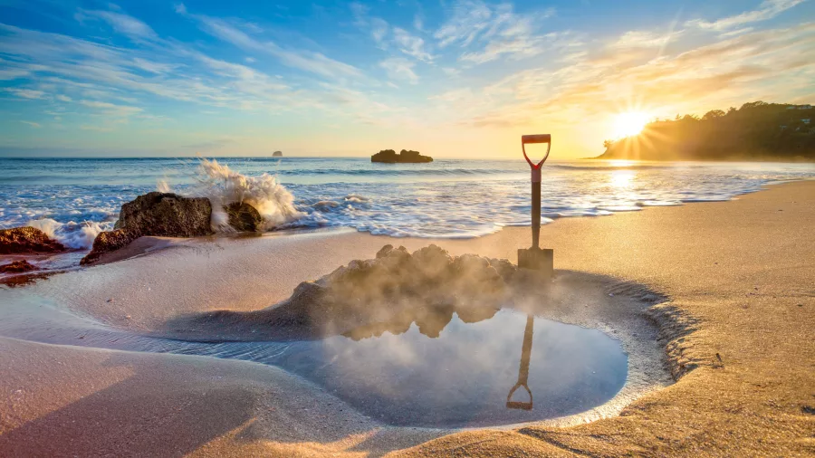 Steaming thermal pool dug into the sand at sunrise on Hot Water Beach, a famous geothermal attraction on the Coromandel Peninsula, New Zealand