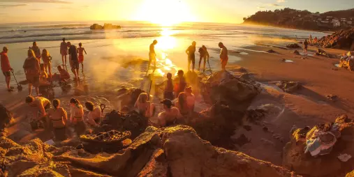Crowds digging steaming thermal pools in the sand at sunrise on Hot Water Beach, a famous geothermal attraction on the Coromandel Peninsula, New Zealand