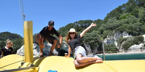 Guests smiling and posing on the front of the yellow sailing catamaran near Cathedral Cove