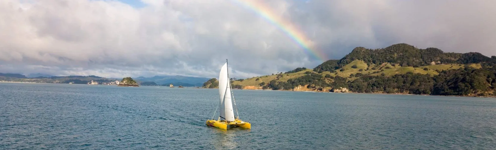 Yellow catamaran sailing under a rainbow in Mercury Bay