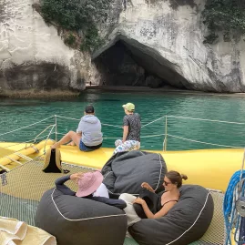 Guests relaxing on beanbags while approaching Cathedral Cove by boat