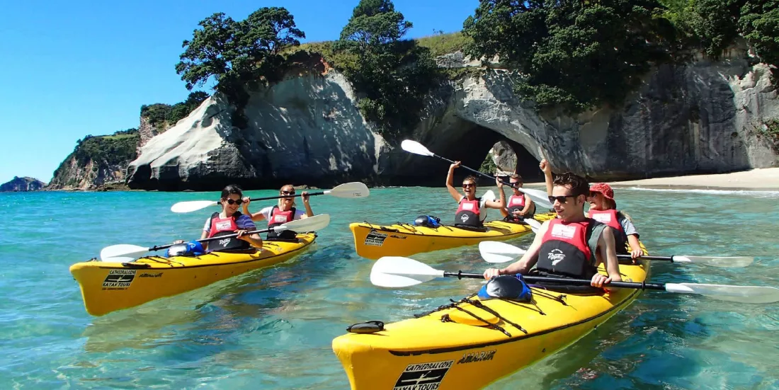 Group of kayakers arriving at Cathedral Cove beach with archway in background