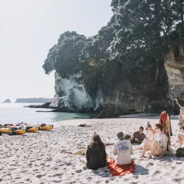 Group of kayakers relaxing on the sand near Cathedral Cove with kayaks on the shore