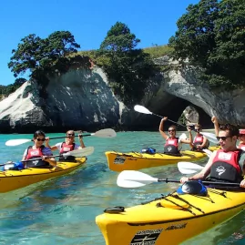 Group of kayakers arriving at Cathedral Cove beach with archway in background