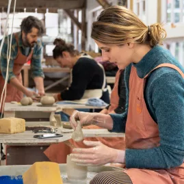 Student shaping clay on a pottery wheel during class at Driving Creek
