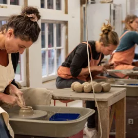 Women shaping clay on wheels during a pottery class at Driving Creek