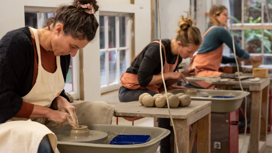 Women shaping clay on wheels during a pottery class at Driving Creek