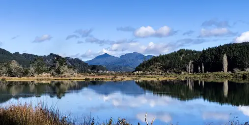 Scenic reflections of forested mountains on a still lake near Pauanui and Tairua on the Coromandel Peninsula, New Zealand