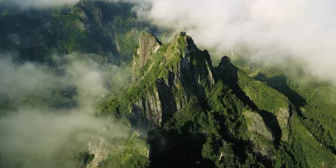 Aerial view of The Pinnacles mountain peaks rising above the forest and clouds in Coromandel Forest Park, New Zealand