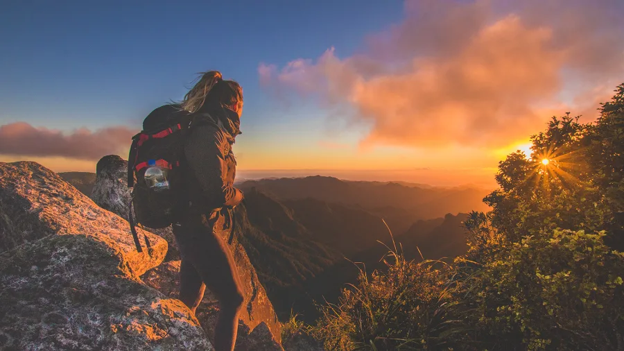 Hiker standing on rocky summit at sunset with mountain views from The Pinnacles in the Coromandel Forest Park, Waikato, New Zealand