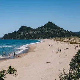 Scenic view of Tairua Beach shoreline with people swimming and relaxing along the sandy coast on the Coromandel Peninsula, New Zealand