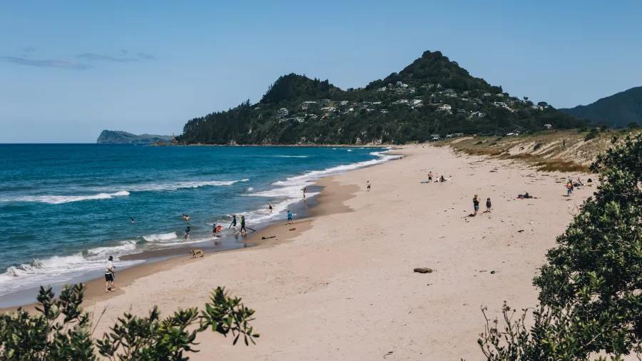 Scenic view of Tairua Beach shoreline with people swimming and relaxing along the sandy coast on the Coromandel Peninsula, New Zealand