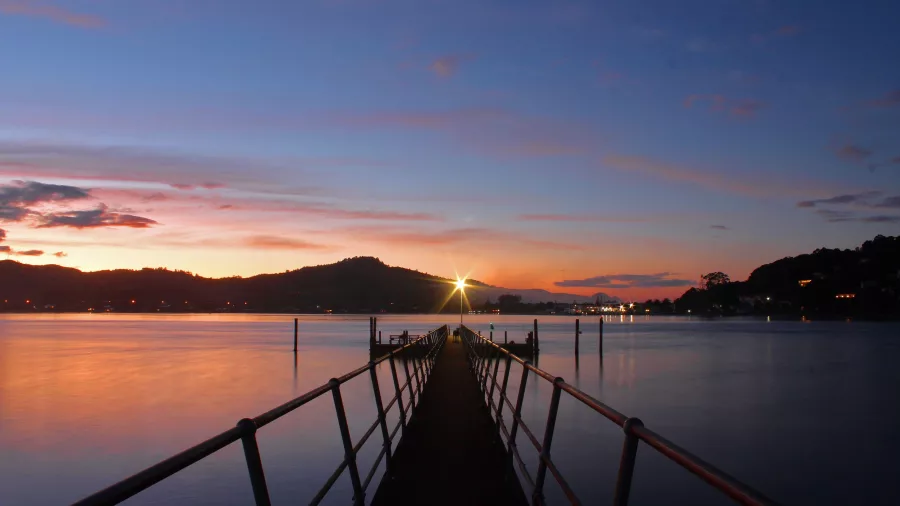 Jetty stretching out into Tairua Harbour at sunset with colourful skies and coastal hills on the Coromandel Peninsula, New Zealand