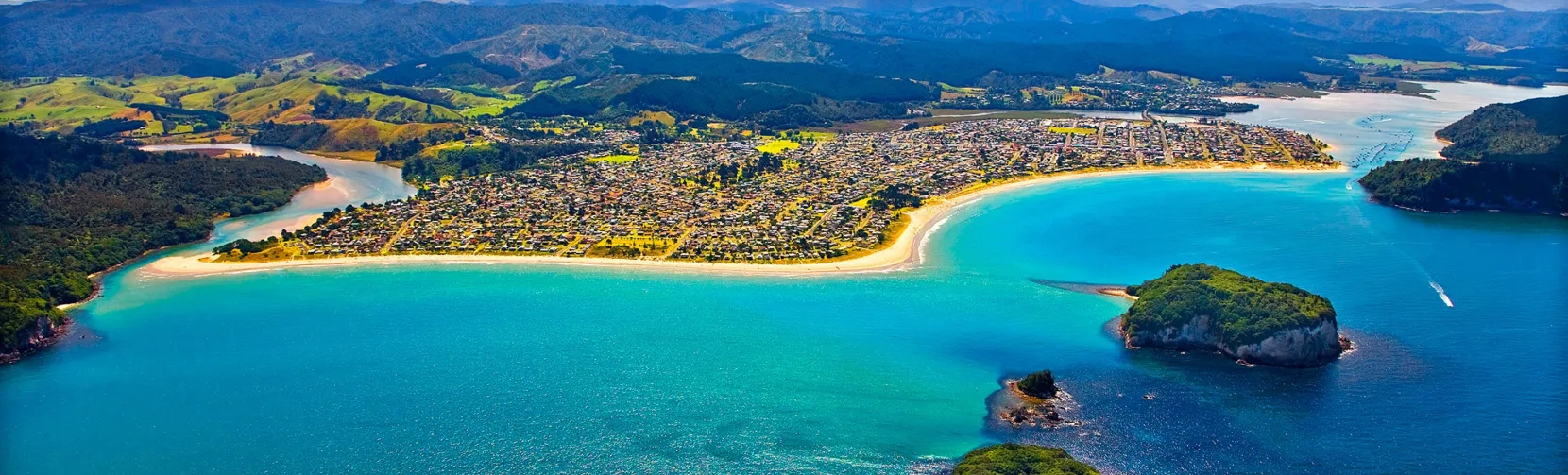 Aerial view of Whangamata Beach with turquoise water, offshore islands, and harbour entrance on the Coromandel Peninsula, New Zealand