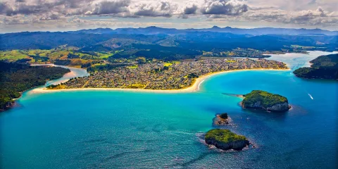 Aerial view of Whangamata Beach with turquoise water, offshore islands, and harbour entrance on the Coromandel Peninsula, New Zealand