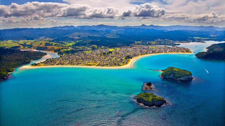 Aerial view of Whangamata Beach with turquoise water, offshore islands, and harbour entrance on the Coromandel Peninsula, New Zealand