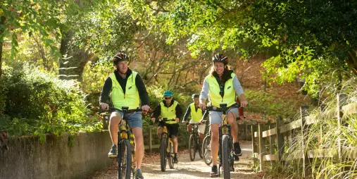 Group of cyclists riding together on a shaded forest trail in high-vis vests