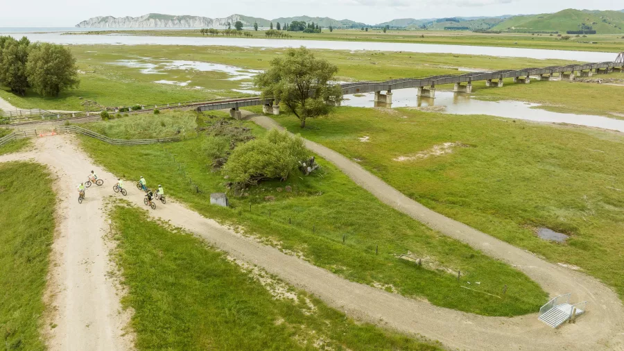 Cyclists regrouping at a trail junction near a river and bridge