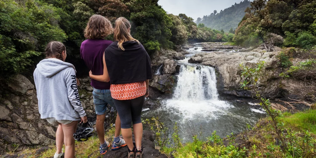 Three people admiring a cascading waterfall surrounded by native bush on the Pakihi Track