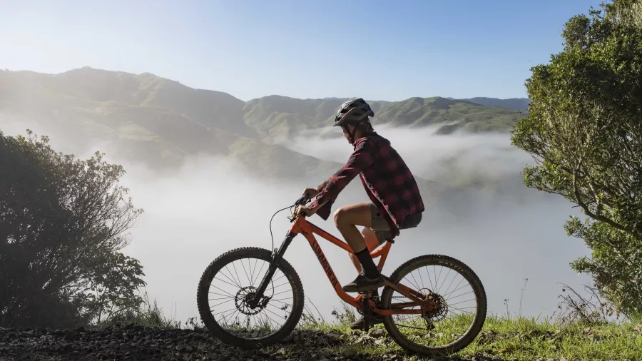 Mountain biker riding along a ridge above the clouds on the Raukumara Traverse