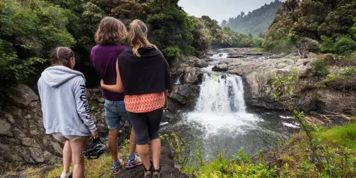 Three people admiring a cascading waterfall surrounded by native bush on the Pakihi Track