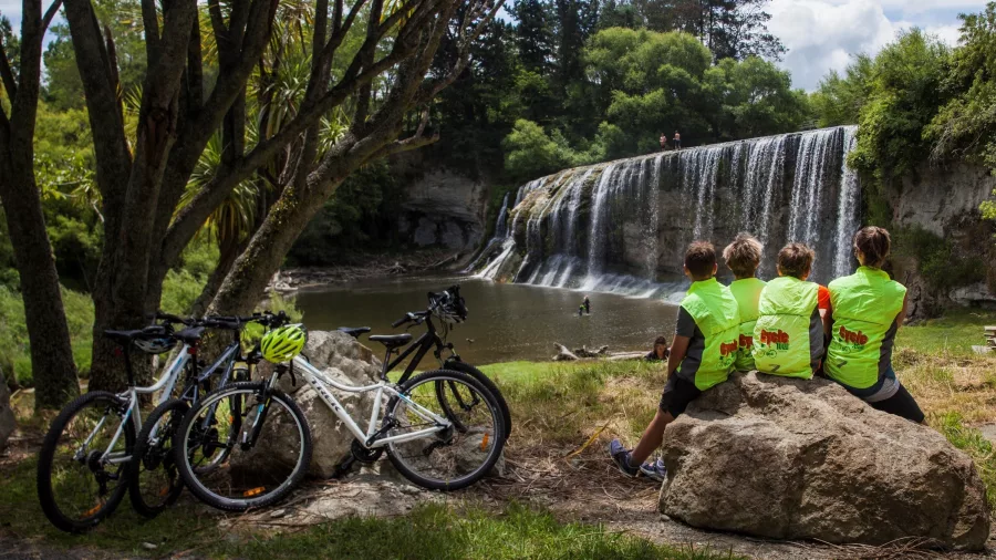 Cyclists resting on rocks near Rere Falls with bikes parked under nearby trees