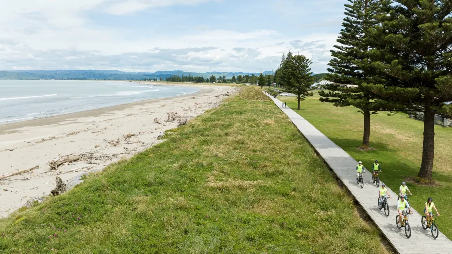 Cyclists riding the boardwalk beside Waikanae Beach on a sunny day
