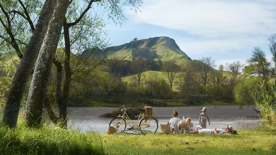Group enjoying a riverside picnic on the grass with bicycles and Te Mata Peak in the background