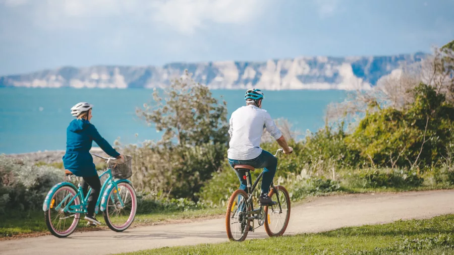 Couple cycling along a coastal path with Cape Kidnappers in the background
