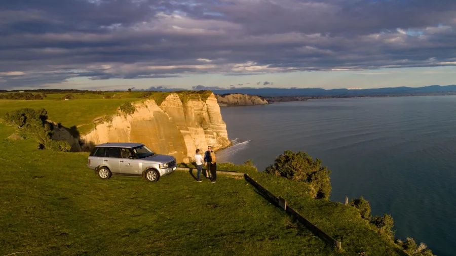 Couple with Range Rover at Cape Kidnappers cliff during private Gannet Safaris tour at sunset
