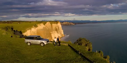 Couple with Range Rover at Cape Kidnappers cliff during private Gannet Safaris tour at sunset