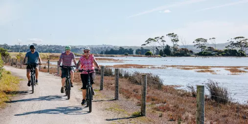 Three cyclists riding along a flat gravel trail beside on the water ride in the Hawke’s Bay wetlands