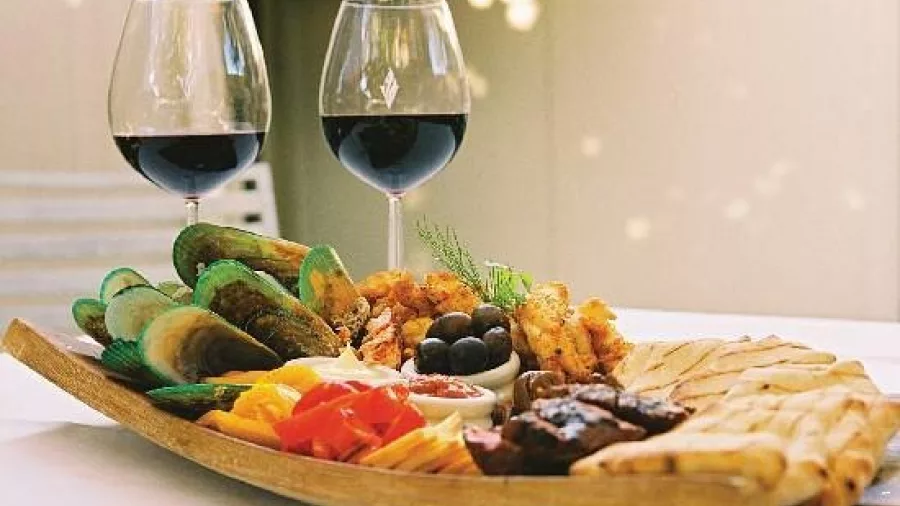 Wooden platter with seafood, cheeses, olives, and two glasses of red wine at a Hawke’s Bay winery