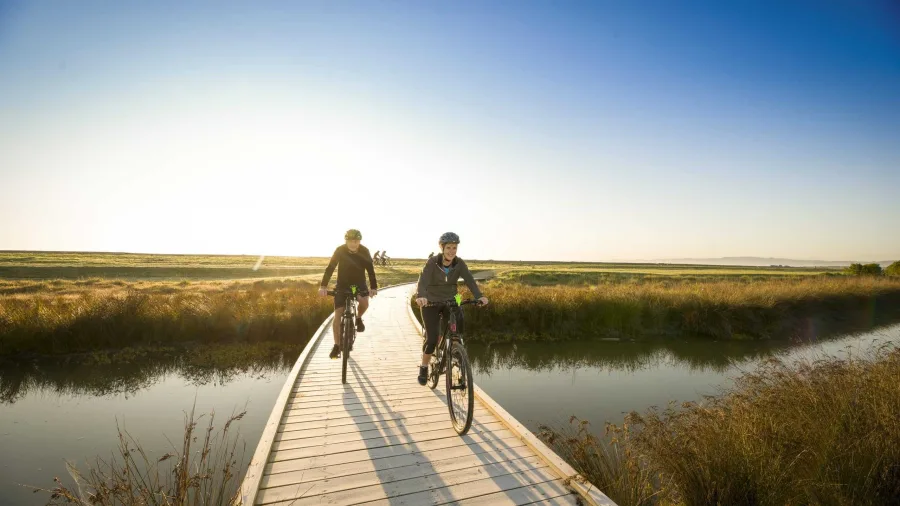 Cyclists riding a boardwalk at sunset along the Water Ride section of the trail