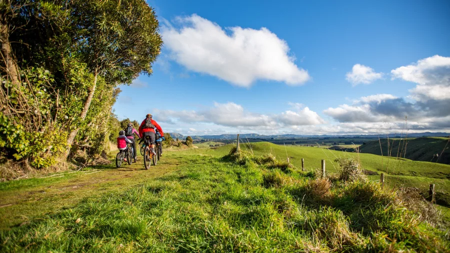 Family biking the Old Coach Road trail near Taumarunui with views over green farmland