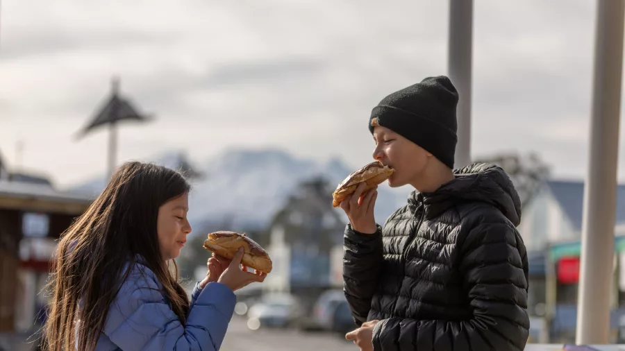 Children enjoying giant chocolate eclairs in Ohakune with snow-covered Mount Ruapehu behind