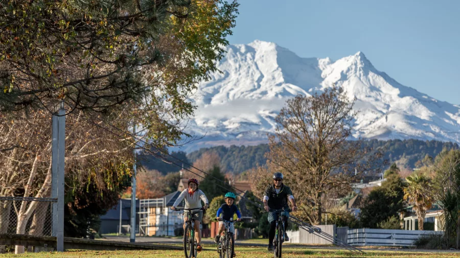 Family riding bikes in Ohakune with snow-covered Mount Ruapehu behind them
