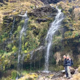 Couple standing in front of lush Soda Springs waterfall on the Tongariro Crossing track